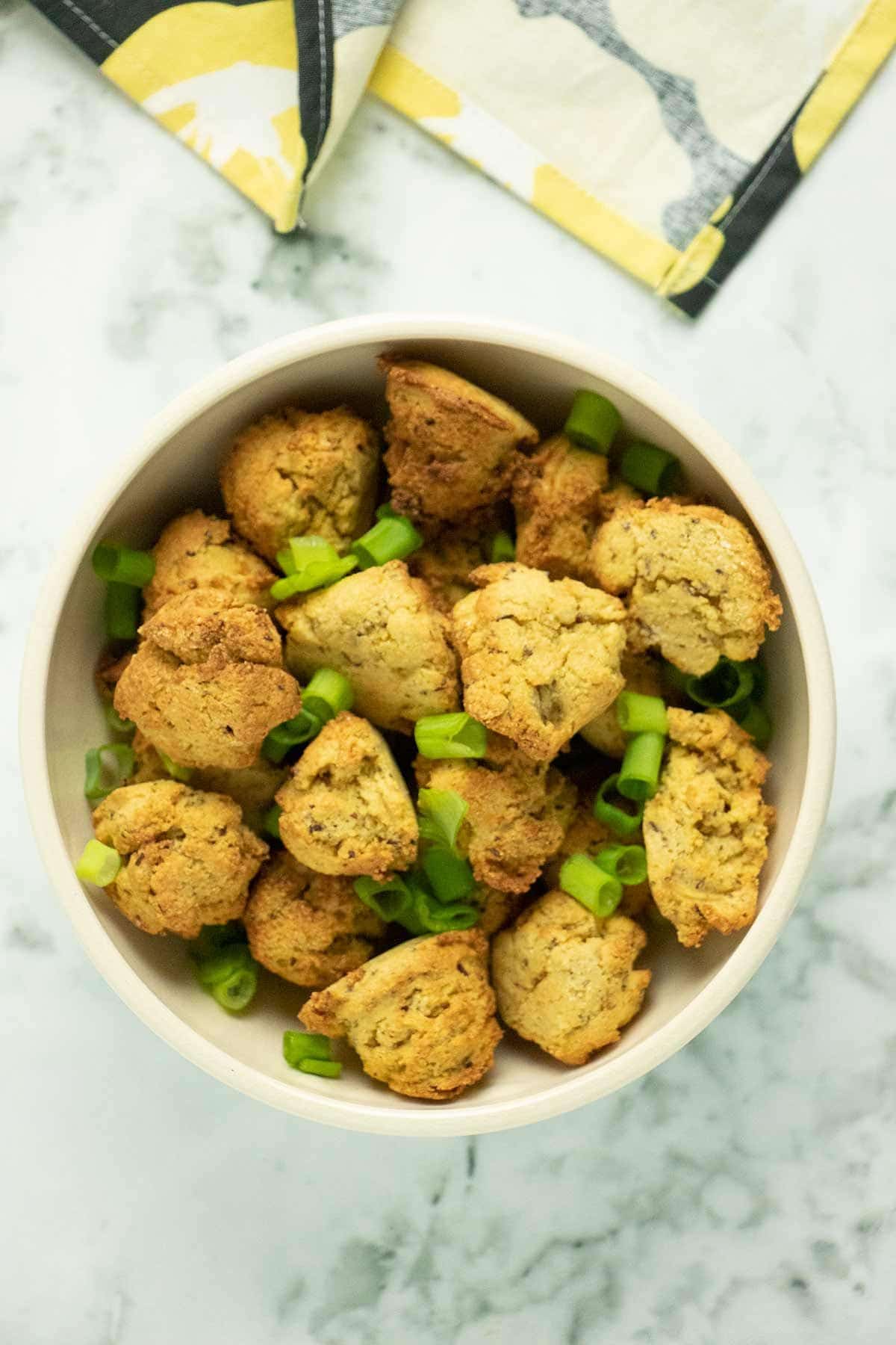 looking down at a white bowl full of potato balls and chopped scallions