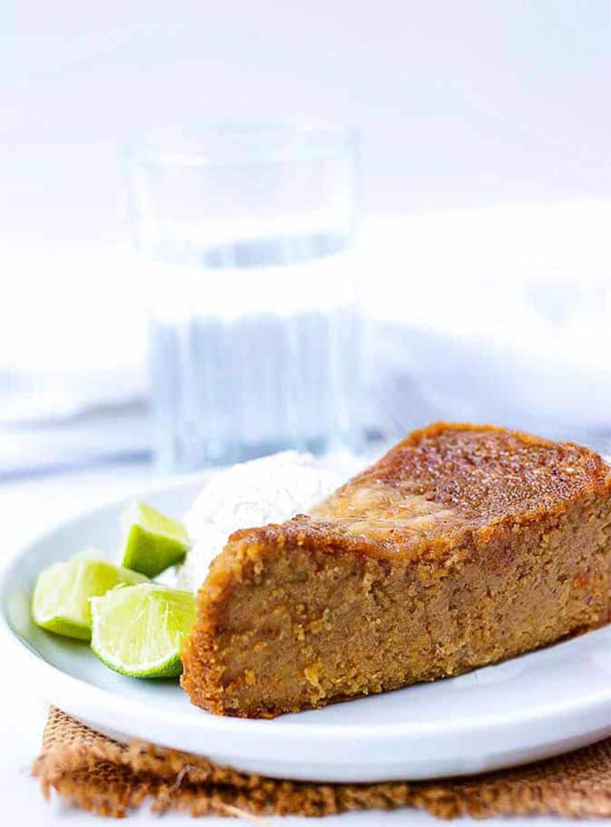 A portion of sweet potato pudding on a white plate next to some lime slices