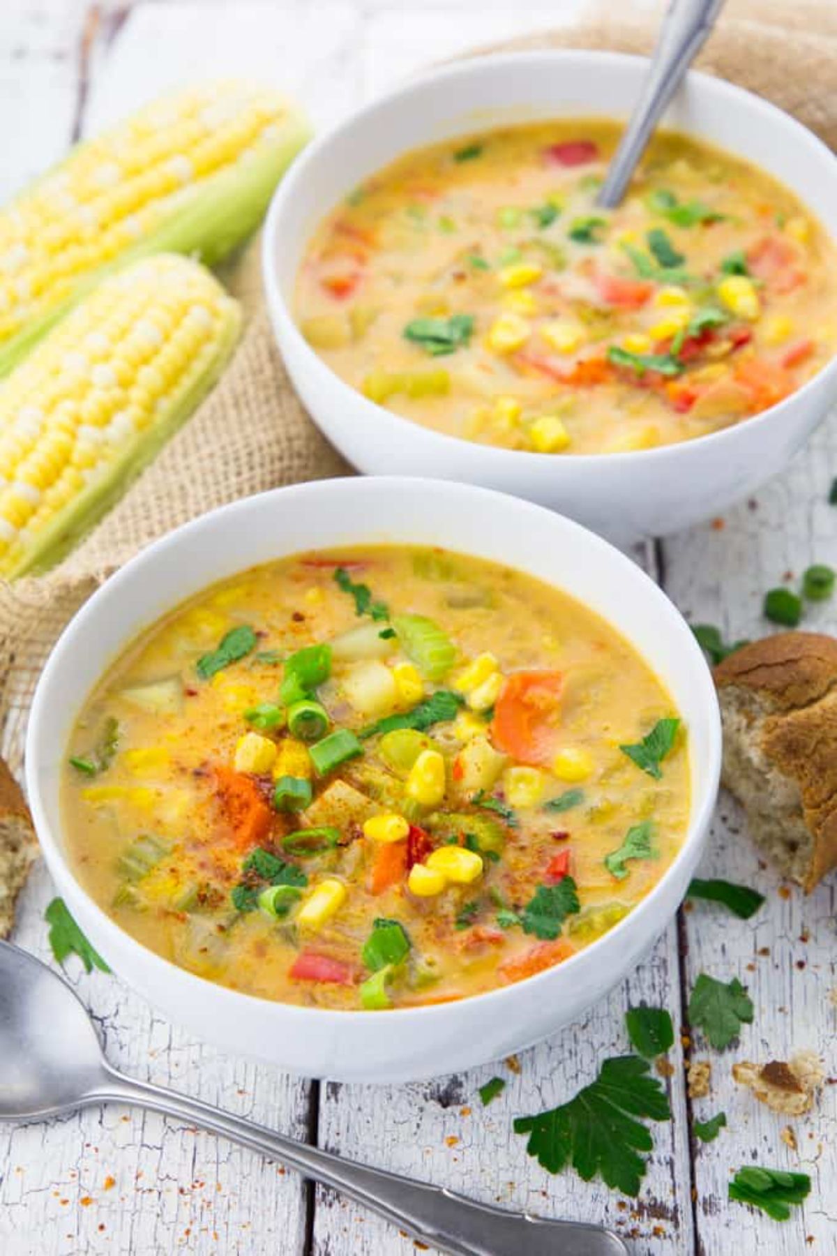 2 bowls full of vegan corn chowder. ears of corn sit behind