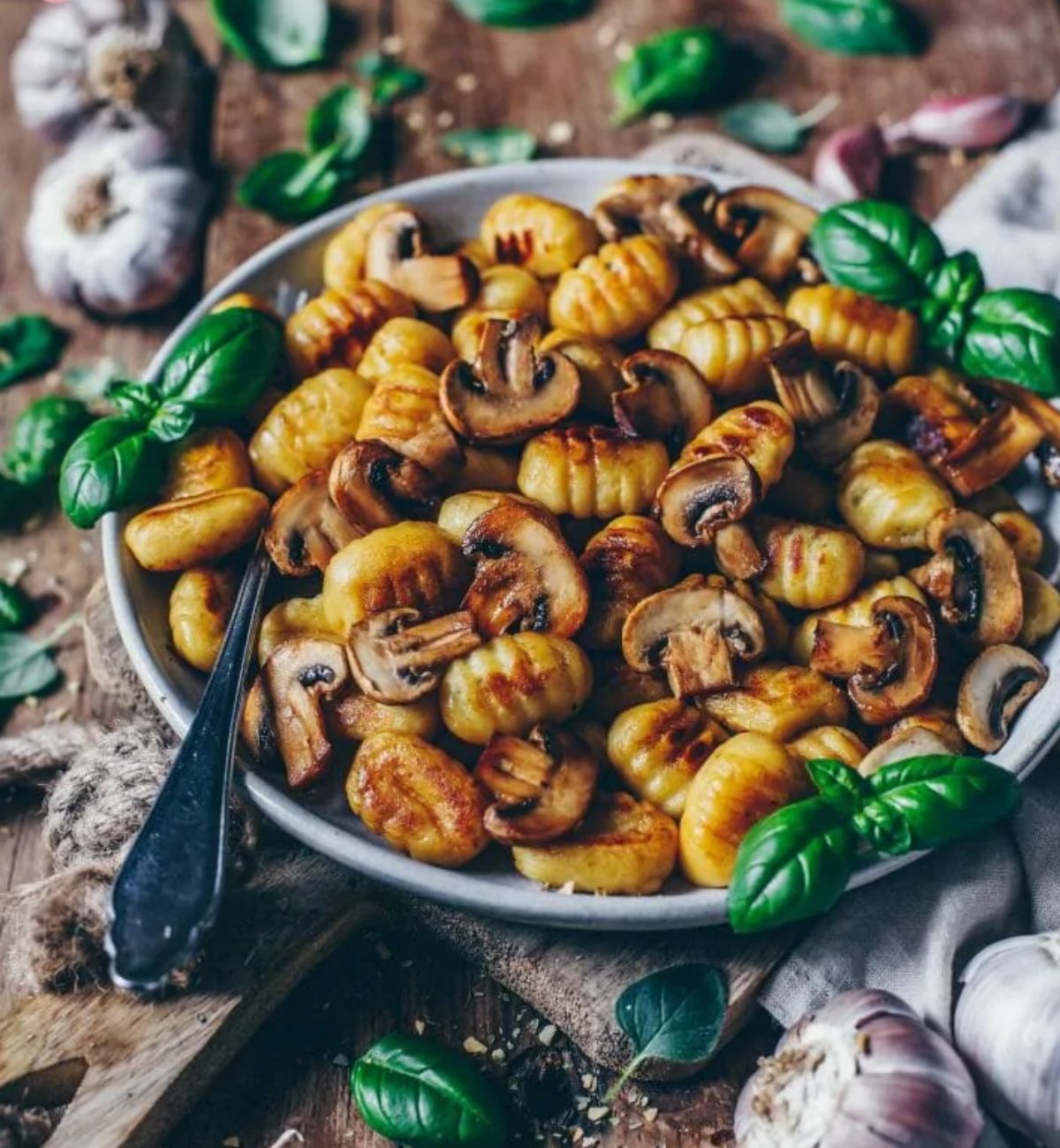 a plate of crispy roasted gocchi with garlic mushrooms, scattered with basil leaves