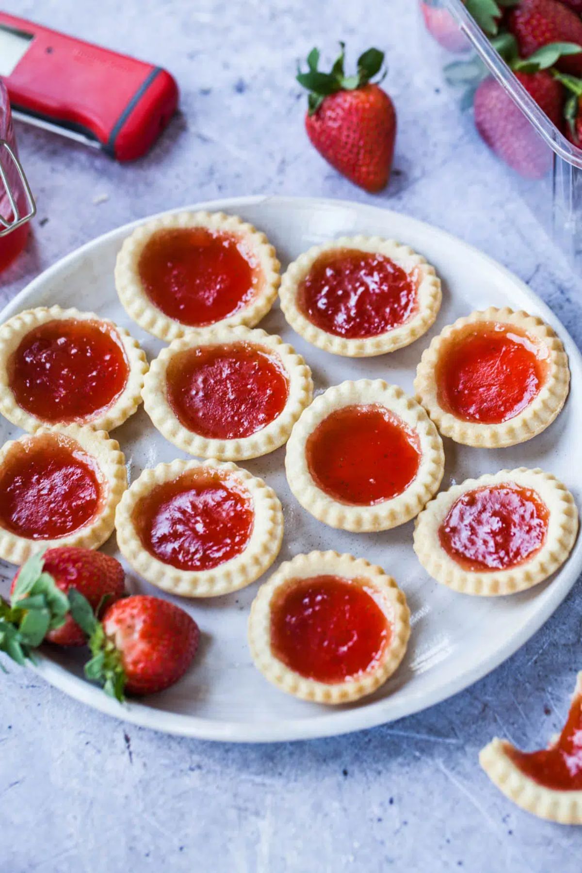 a white plate of jam tarts with strawberries scattered around
