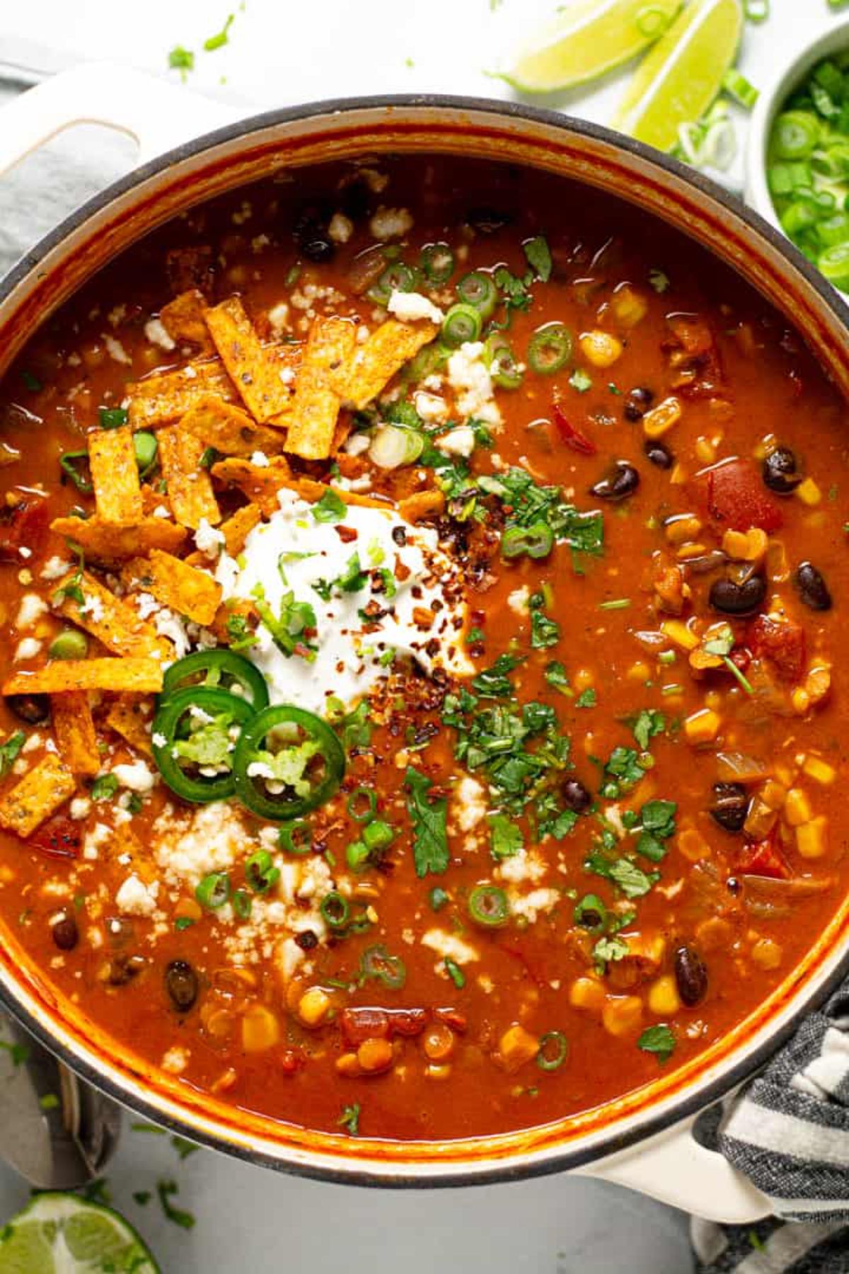 a pan full of lentil tortilla soup topped with chopped herbs, sliced tortillas and jalapeno slices