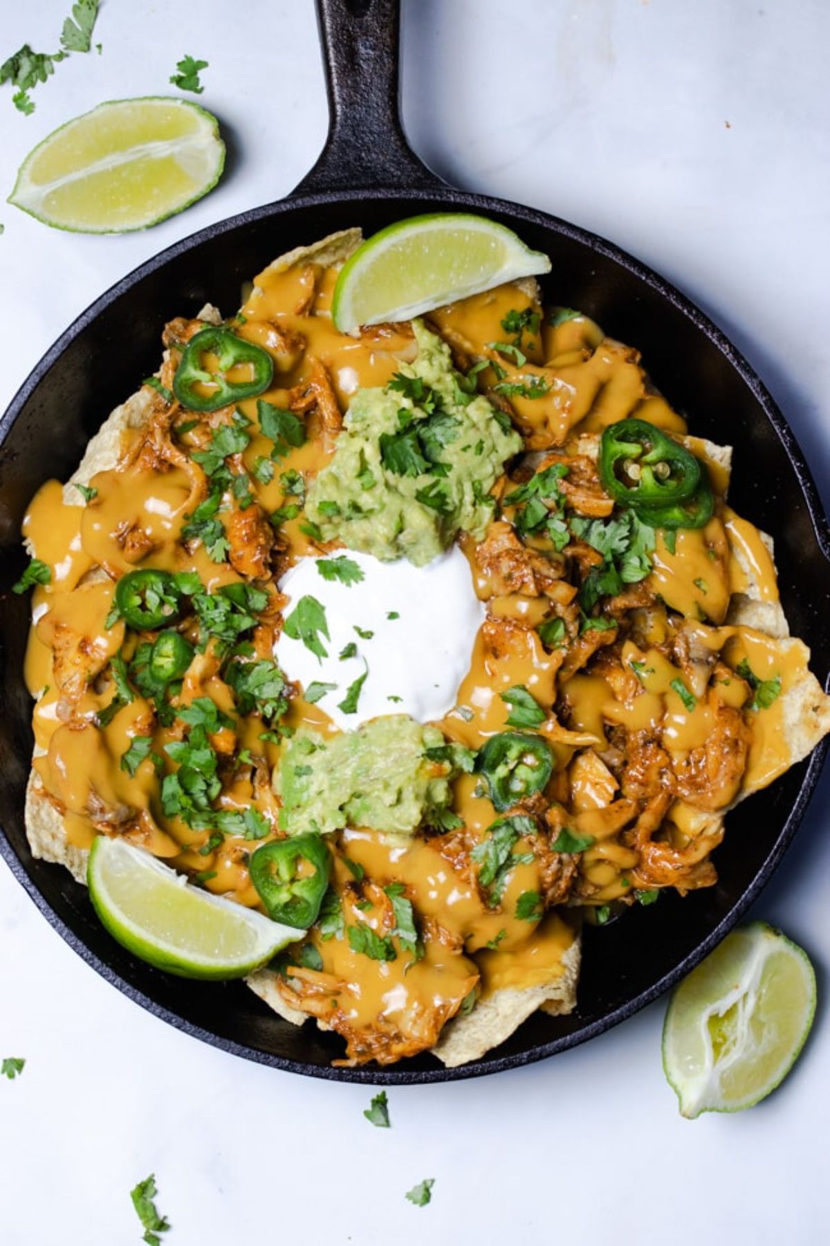 a cast iron skillet of oyster mushroom bachos topped with vegan sour cream, guacamole, and lime wedges