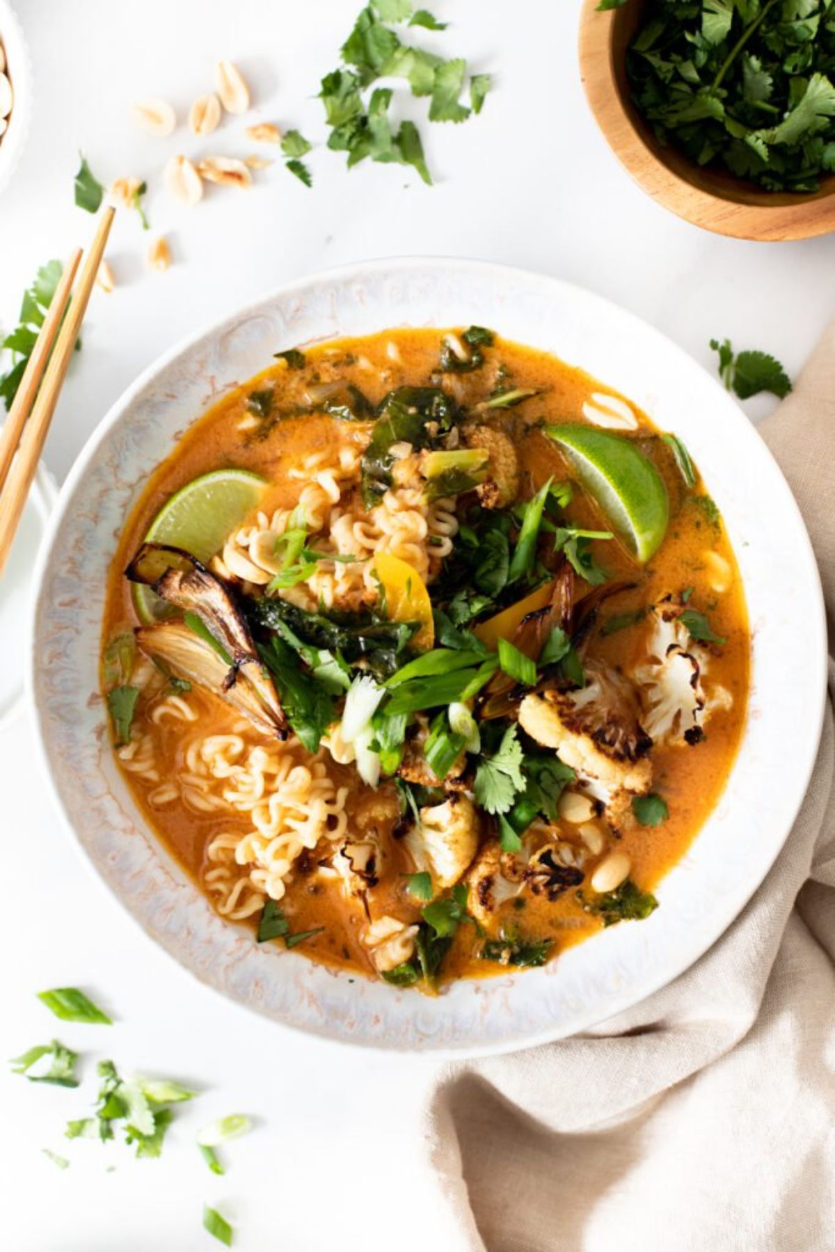 Thai peanut ramen in a whote bowl topped with fresh chopped coriander and peanuts