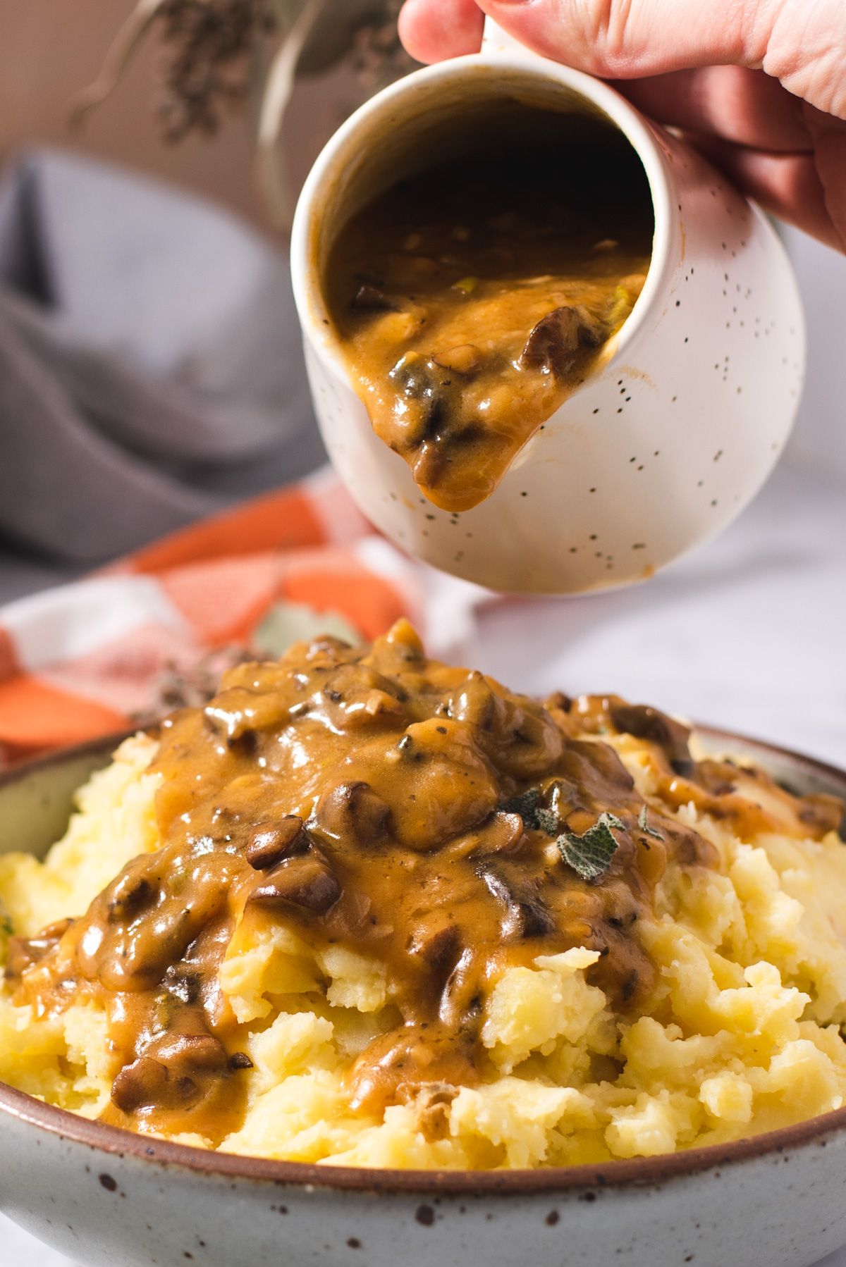 a jug of mushroom gravy being poured onto a plate of mashed potato