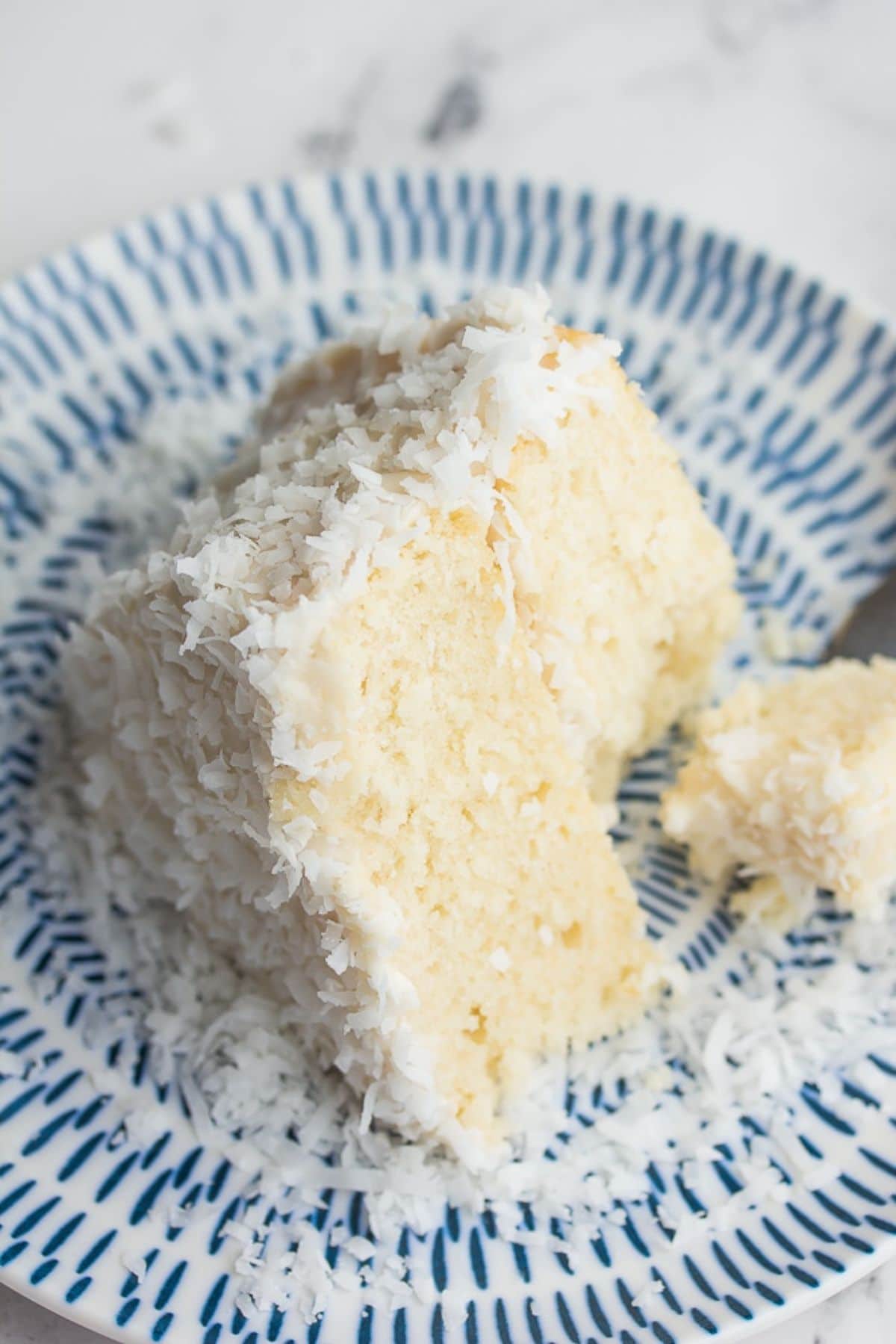 a slice of coconut cake on a blue and white plate with a bote taken out of it