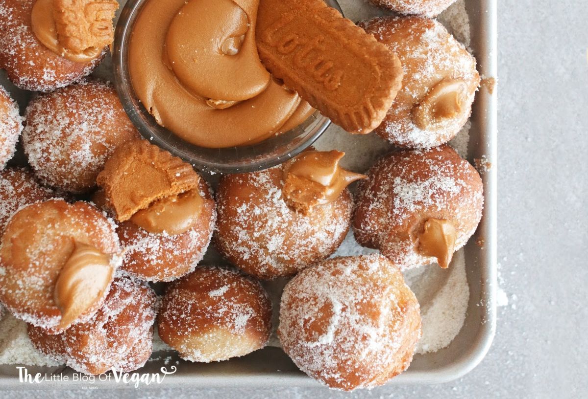 a baking rray of donut holes filled with biscoff spread. in the middle is a glass bowl of biscoff spread with a biscoff biscuit sticking out of it