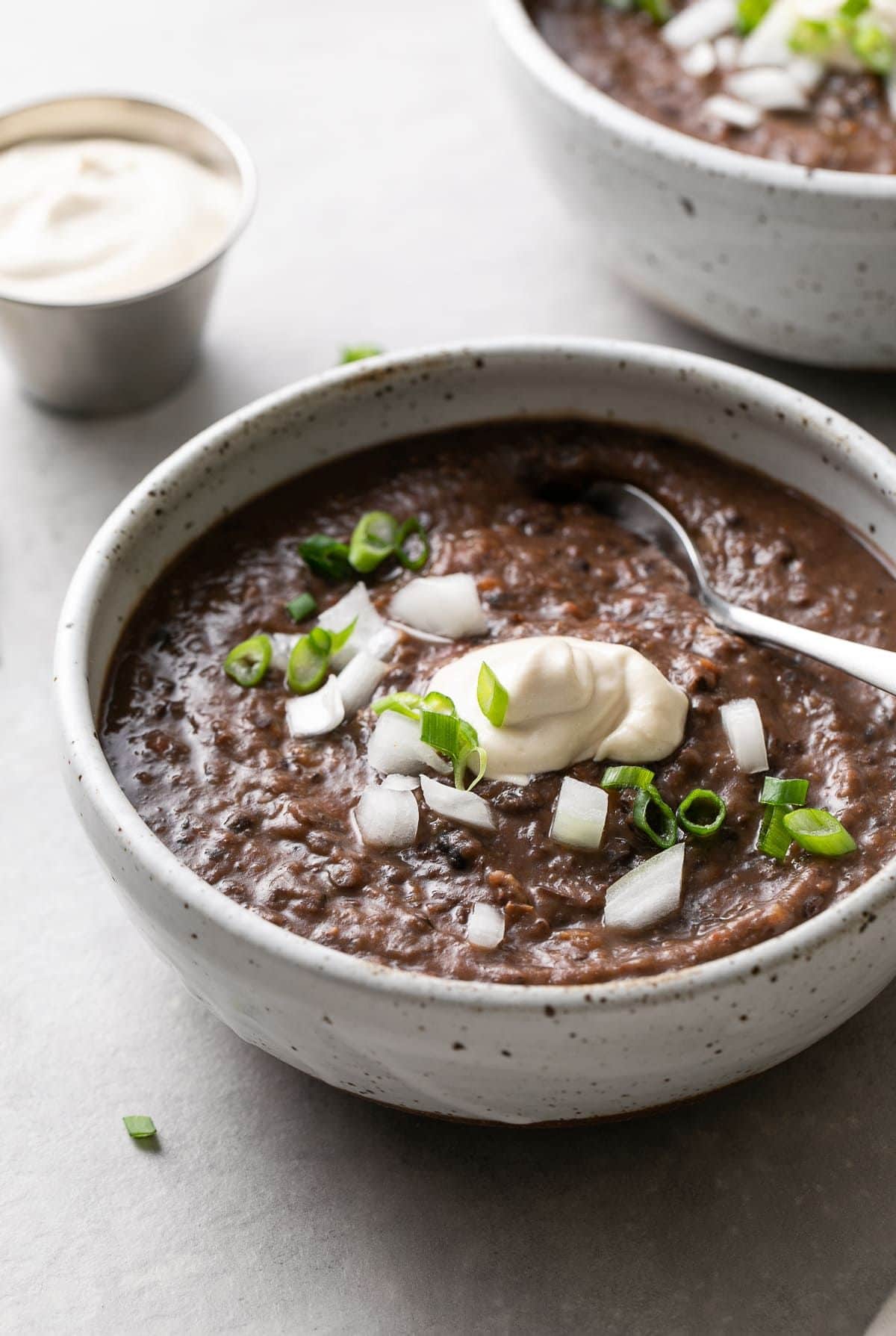 a white bowl full of black bean soup topped with vegan cream and sliced scallions