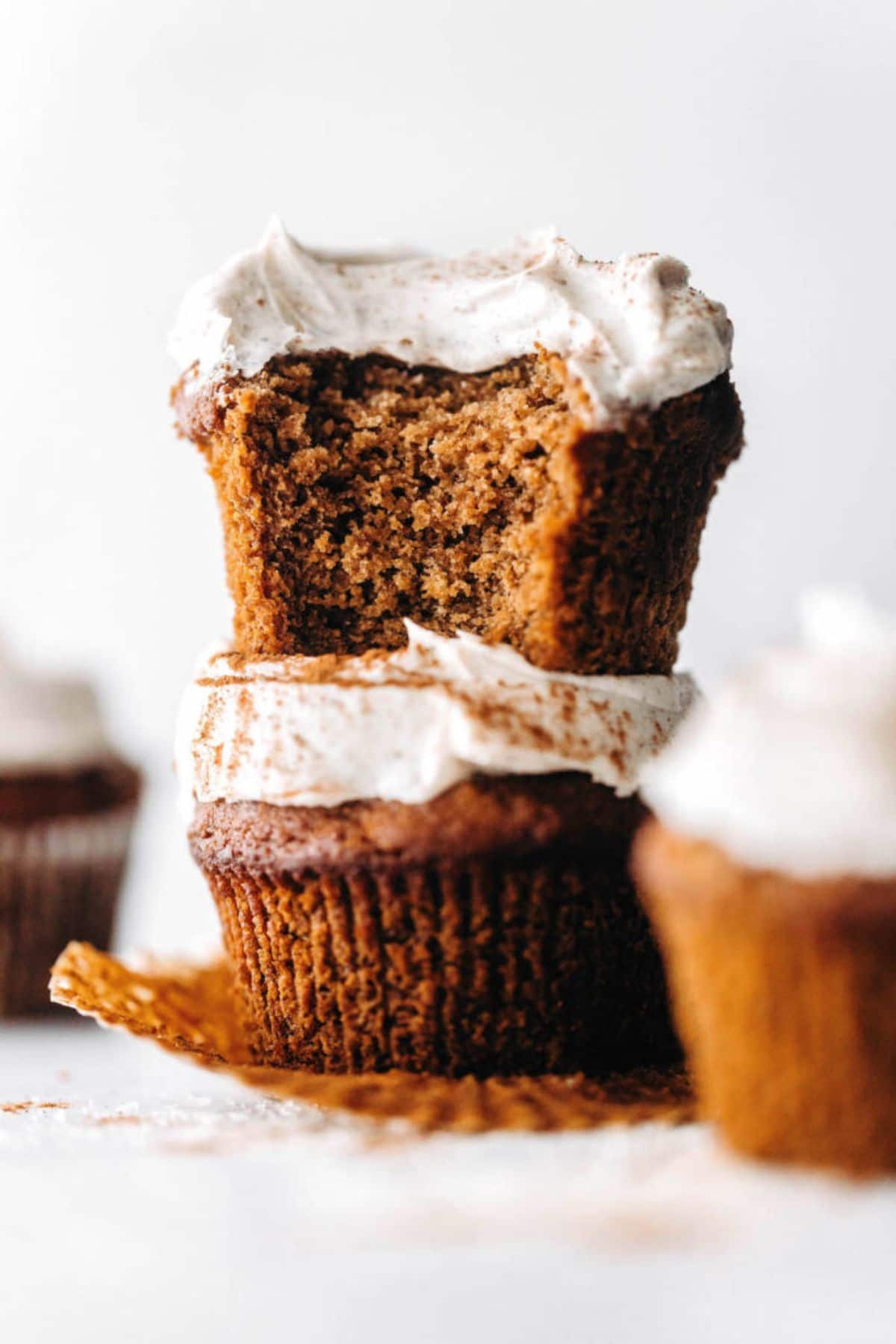 2 vegan chai spiced cupcakes with cegan icing stacked on top of each other. A bite has been taken out of the top one