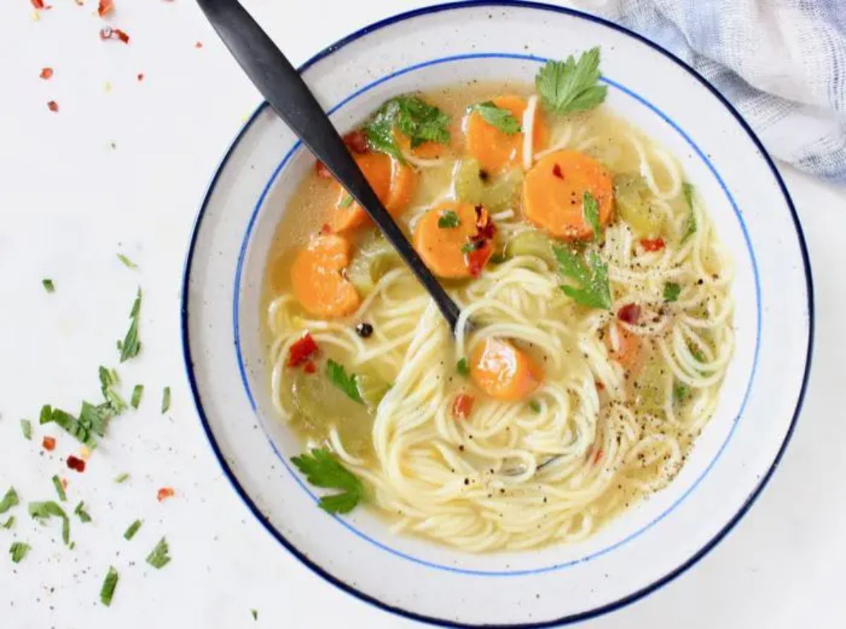 a bowl full of vegetable noodle soup with a spoon sticking into it