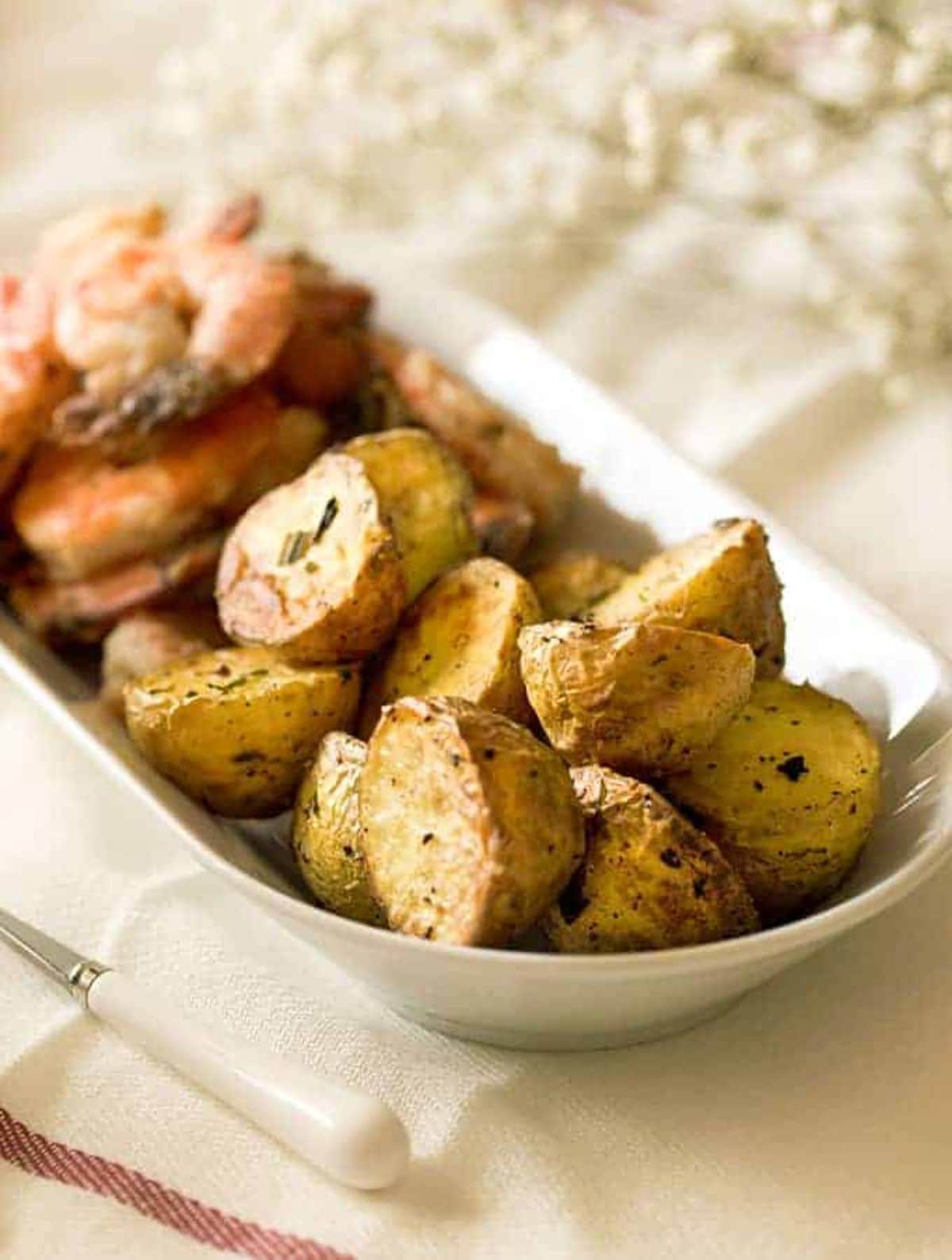 an oval dish full of roast potatoes scattered with rosemary