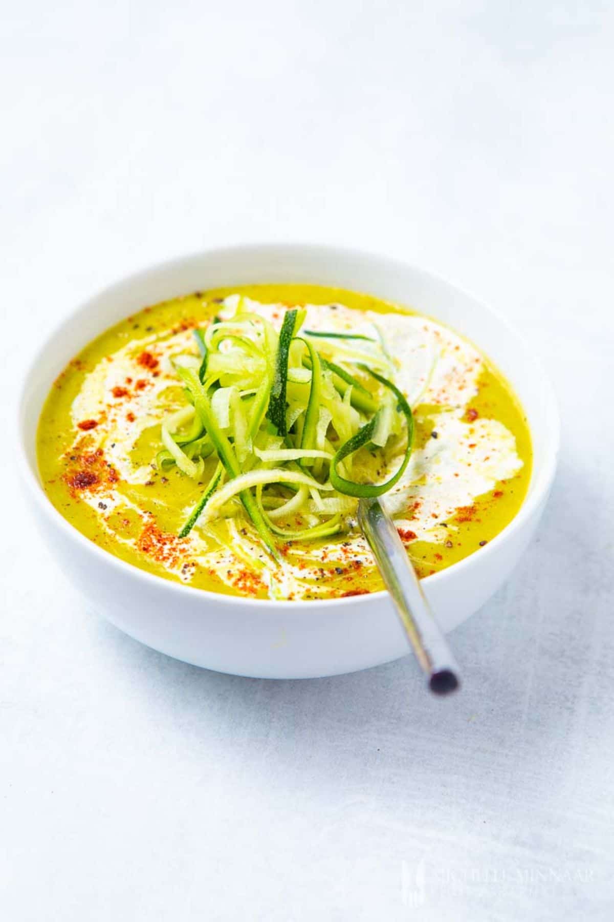 a white bowl full of zucchini and leek soup, topped with vegan cream