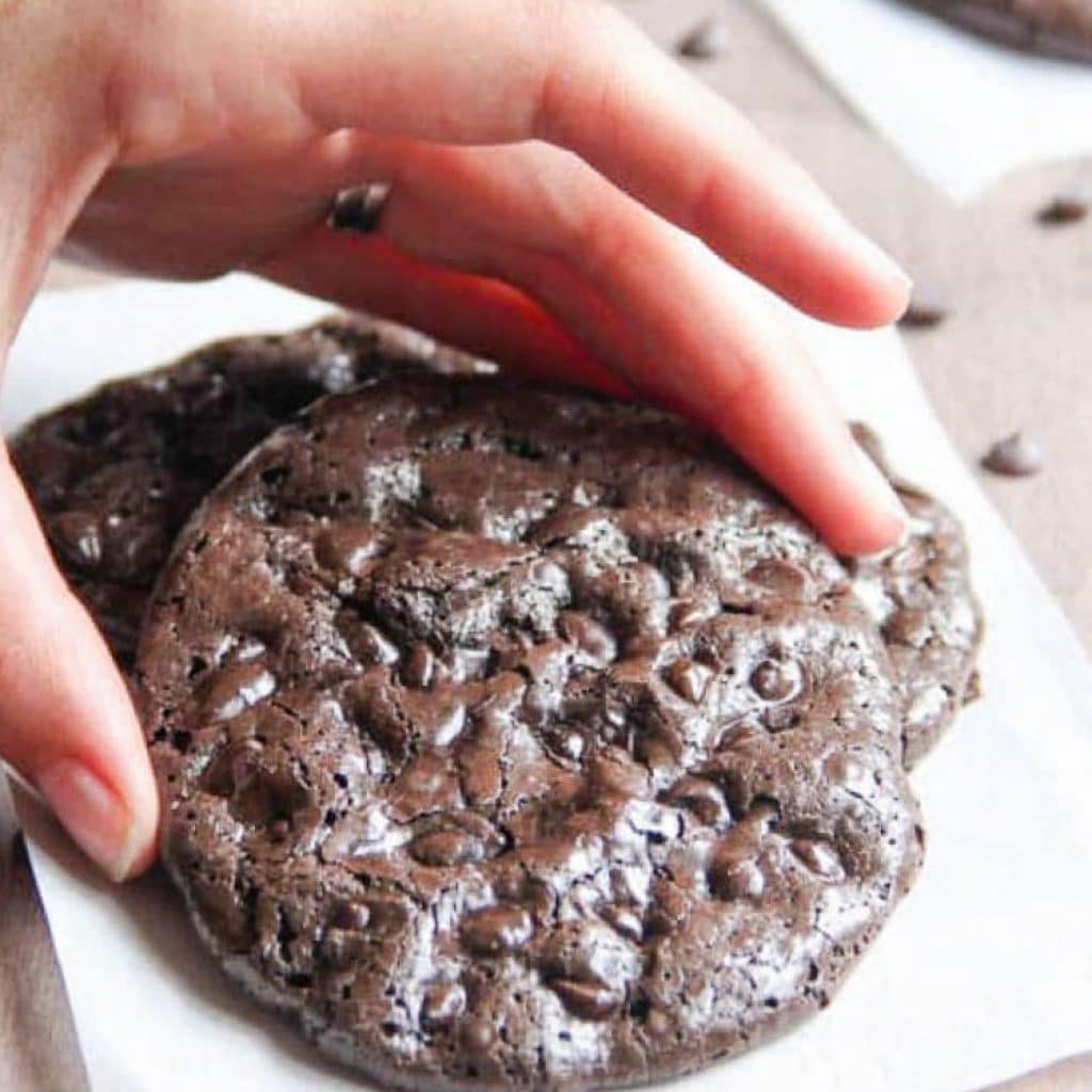 Flourless Double Chocolate Chip Cookies in a pile top one being lifted off.