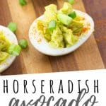 PINTEREST IMAGE with words "Horseradish Avocado Deviled Eggs" Horseradish Avocado Deviled Eggs on a wooden cutting board with green onion sprinkled over top