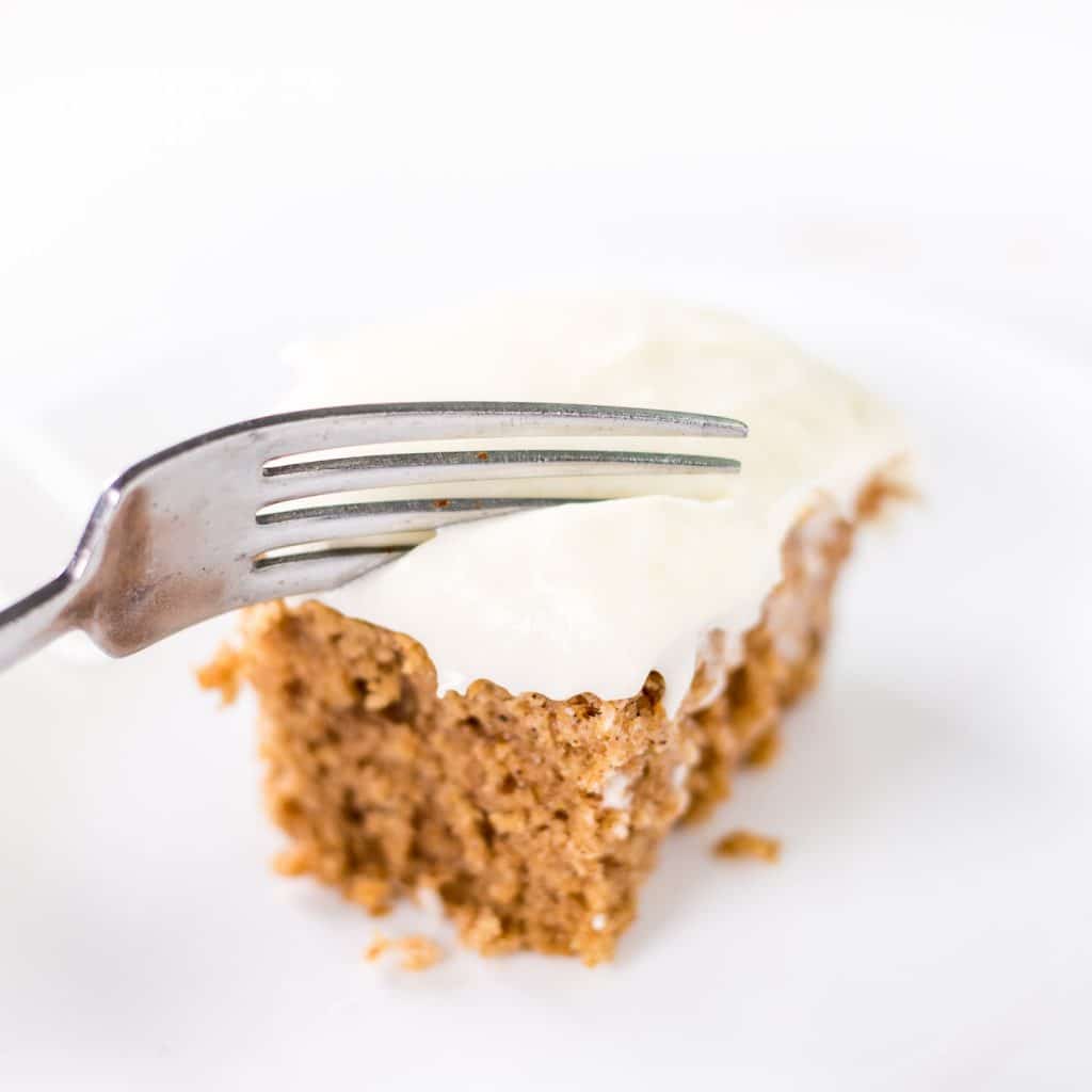 Applesauce Spice Cake slice with white icing on top being cut into with a fork