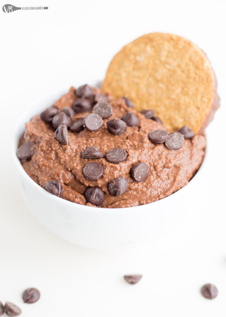 Brownie Batter Chocolate Hummus in small white bowl with chocolate chips and a cookie on top.
