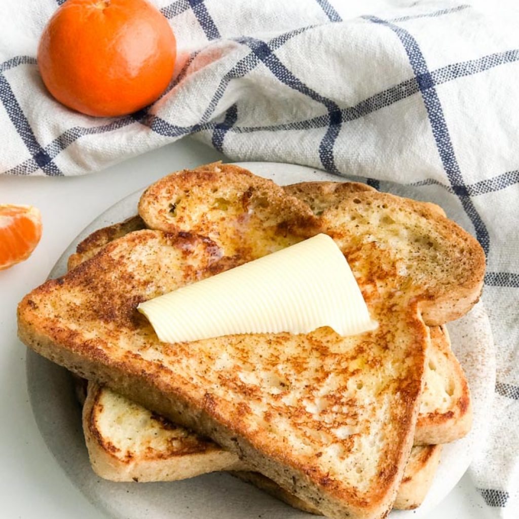 Gluten Free French Toast stacked with butter on top and orange on the side