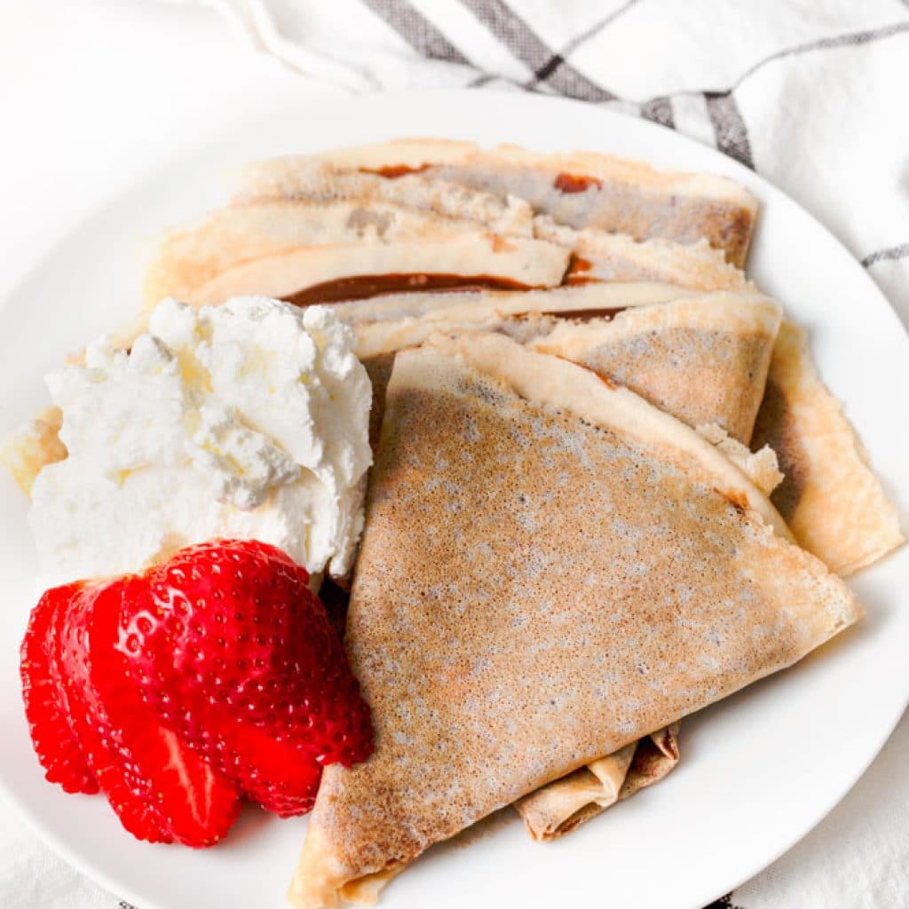 Gluten Free Crepes on a plate with whipped cream and strawberries