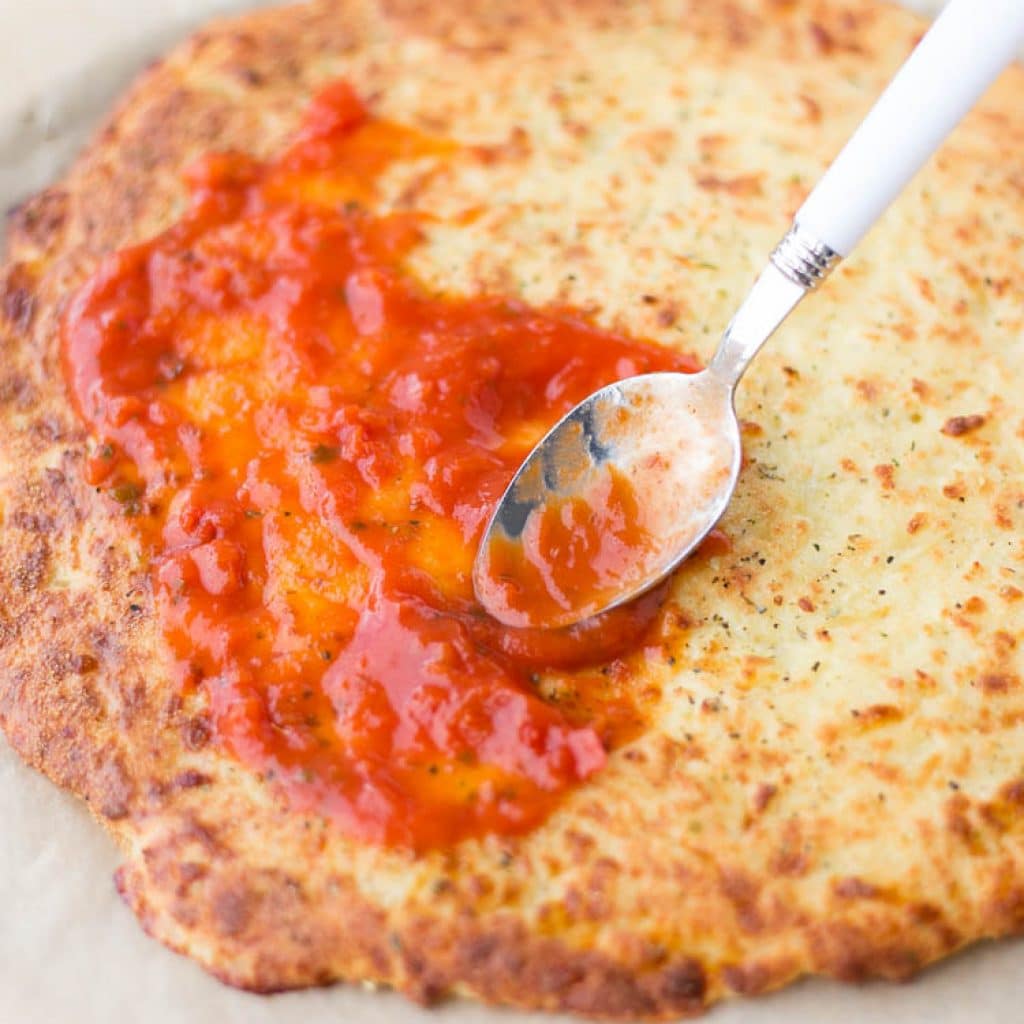 The Best Gluten Free Pizza Crust with marinara being spread on top