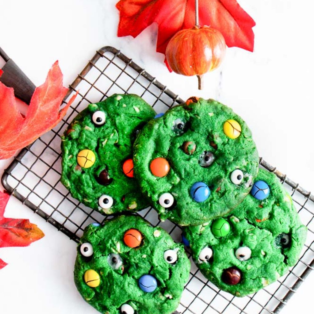 Overhead shot of Halloween Monster Cookies green cookies with M&M's and eye candies on top piled on a cooling rack