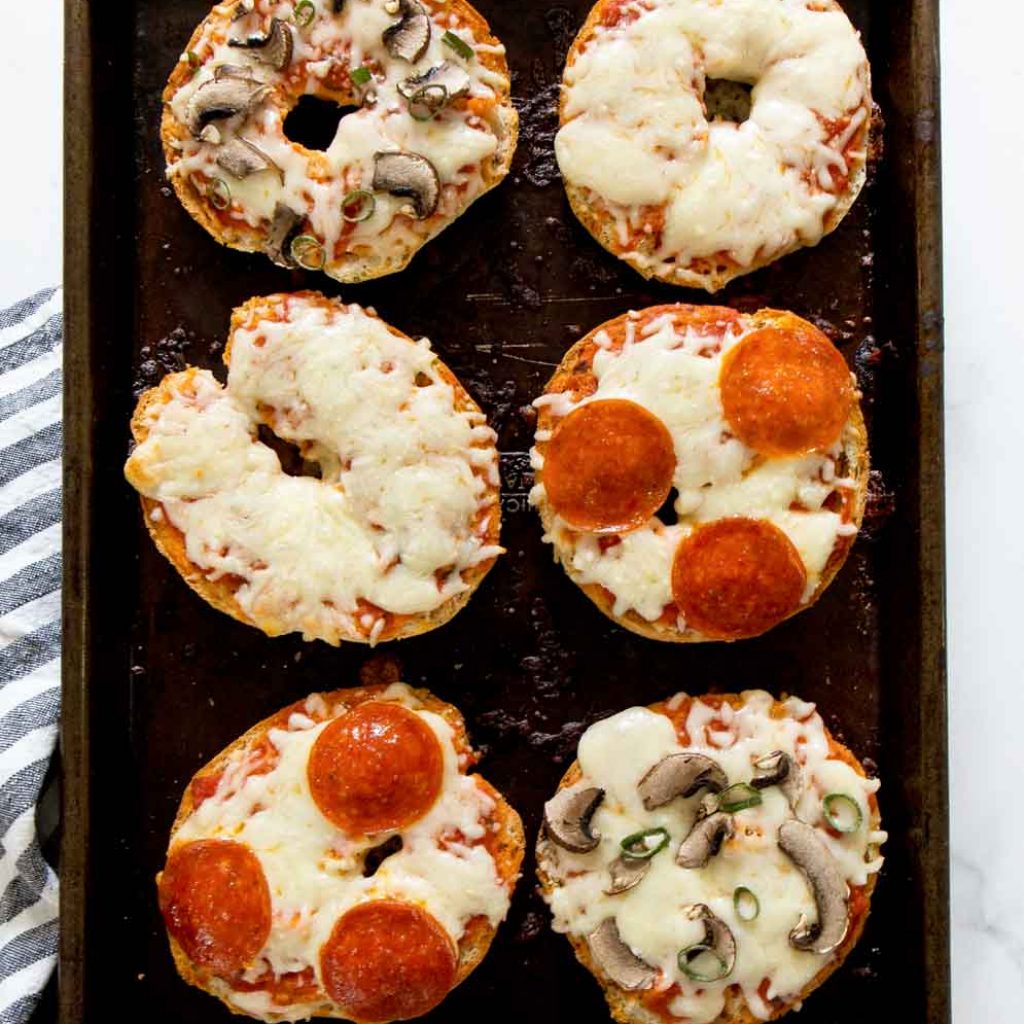 Overhead shot of Gluten Free Pizza Bagels with assorted toppings on a baking sheet