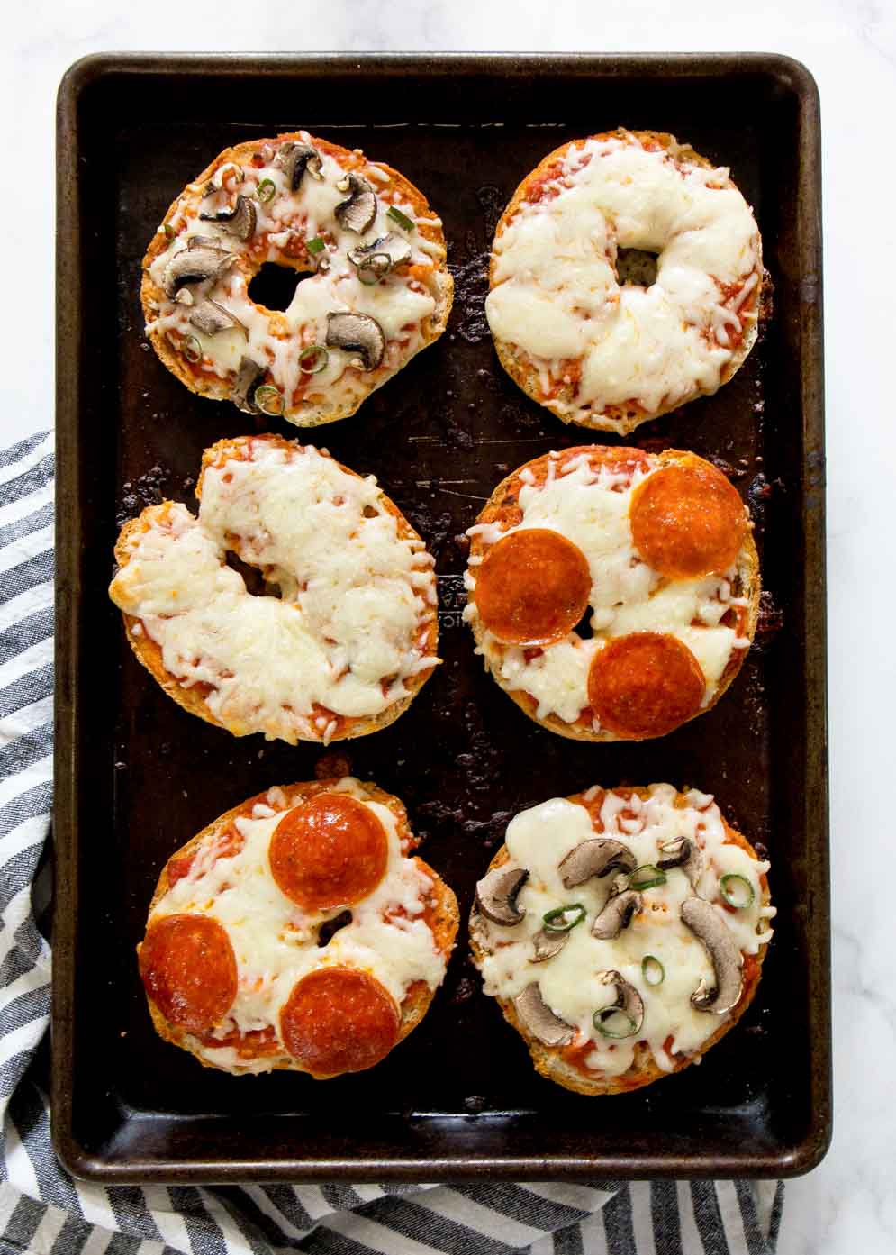 Overhead shot of Gluten Free Pizza Bagels with assorted toppings on a baking sheet