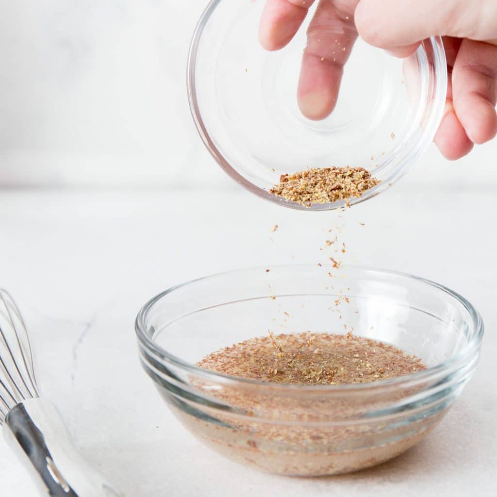 How to Make a Flax Egg flax seed being poured between bowls.