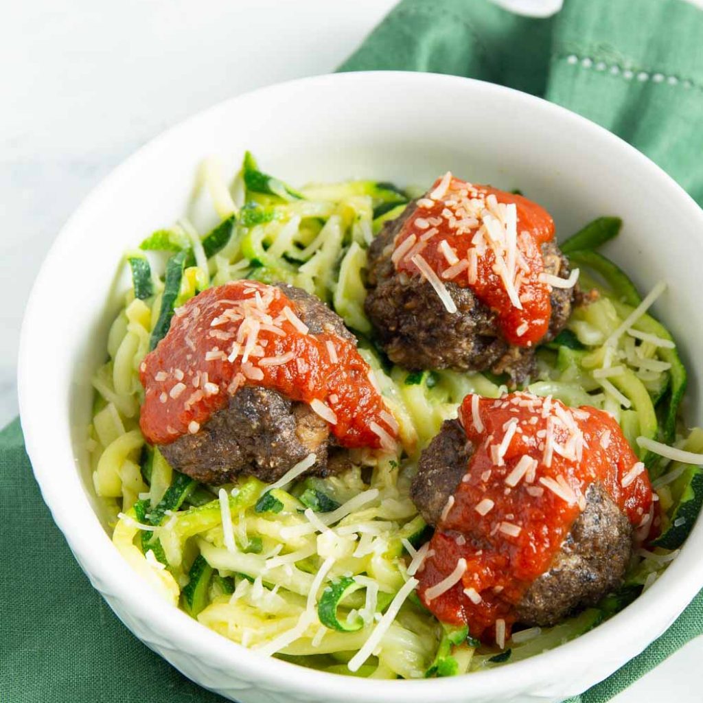 Vegetarian Meatless Meatballs with red sauce on top in a white bowl a top greens