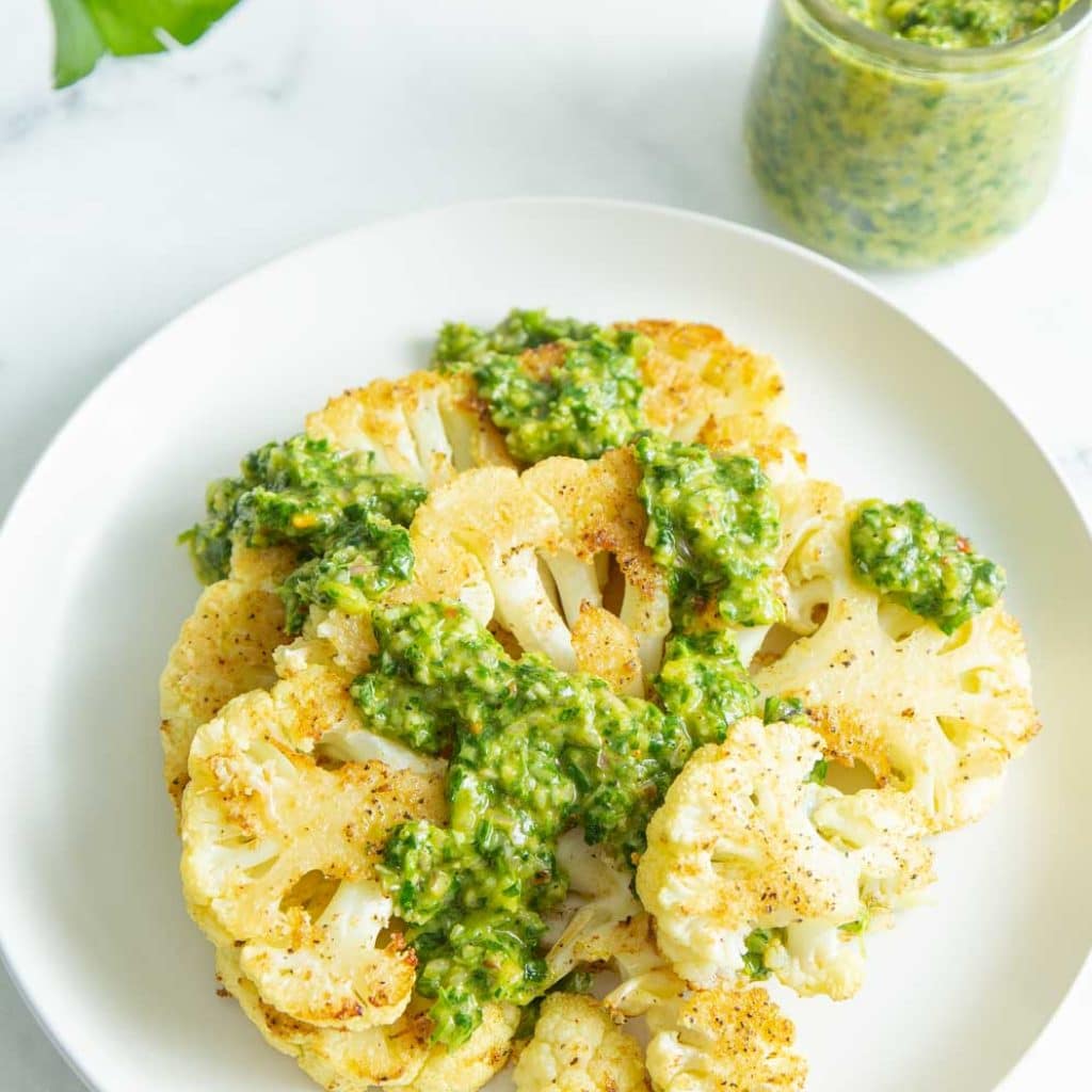 Cauliflower Roasted Steaks on a white plate with chimichurri sauce