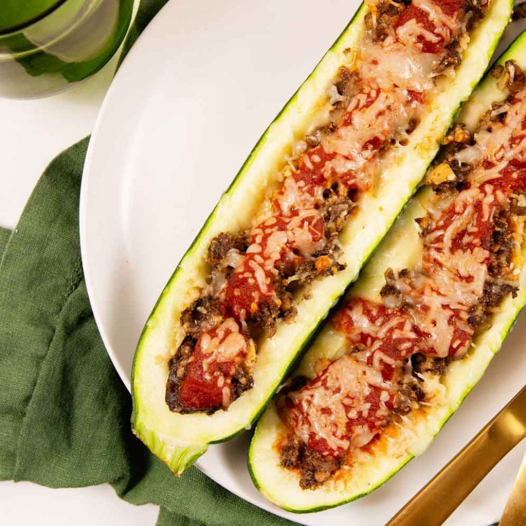 Italian Vegan Stuffed Zucchini Boats on a white plate on a green tea towel