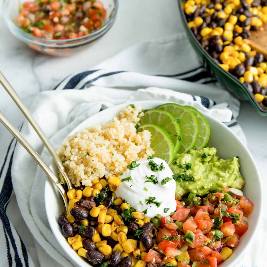 Easy Vegan Burrito Bowl in a white bowl with ingredients in the background