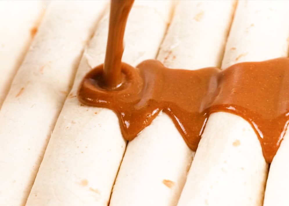 Homemade Red Enchilada Sauce being poured over bean enchiladas