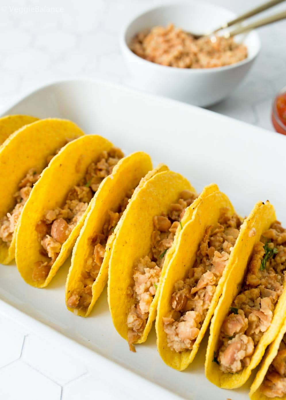 Taco shells stuffed with refried beans as first layer of vegetarian tacos