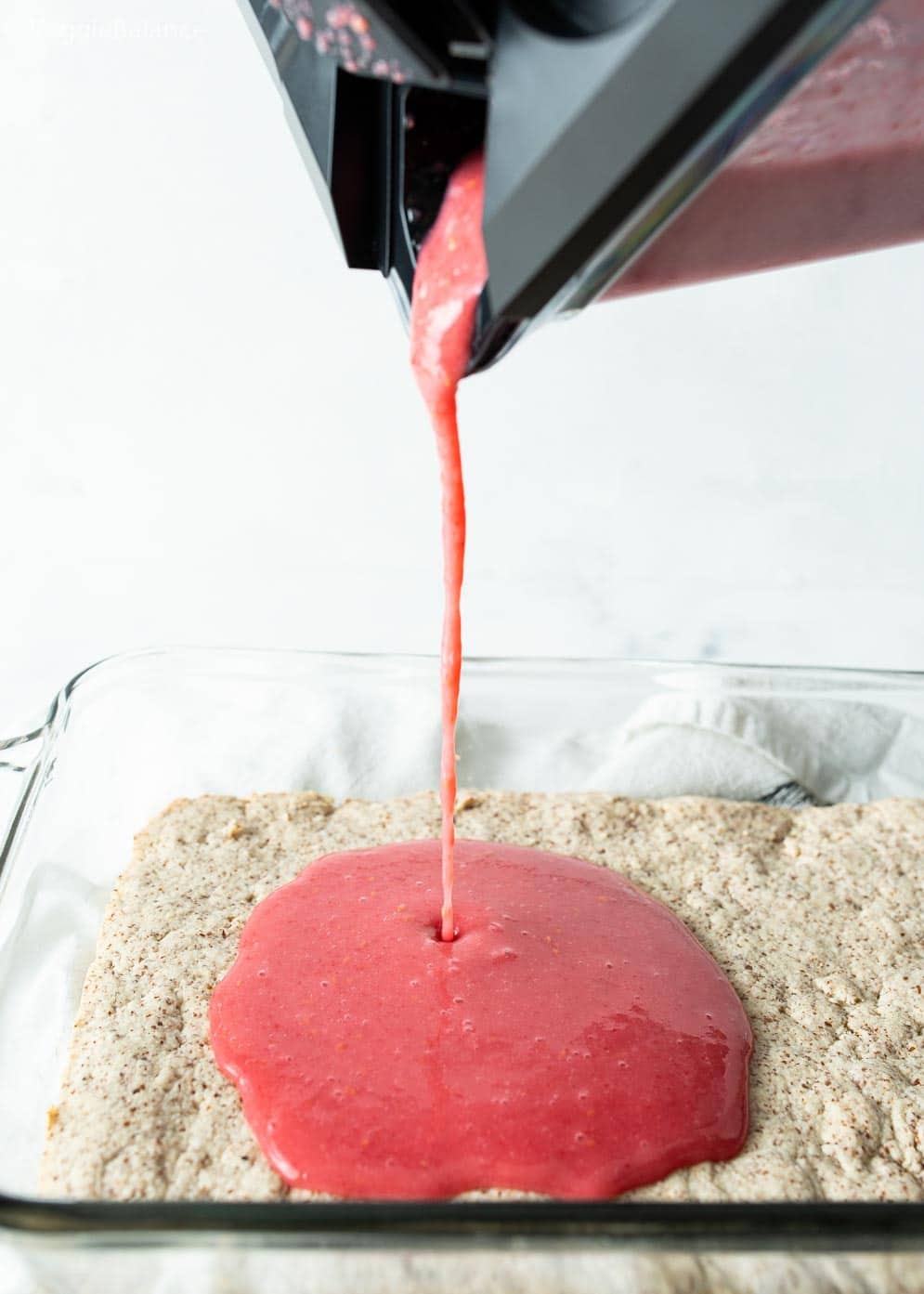 Pour shot of vegan raspberry lemon bar layer being poured onto lemon bar crust