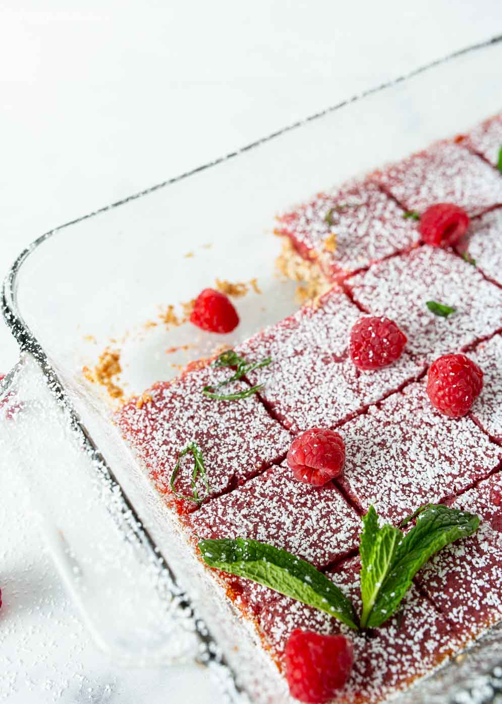 Pan of Vegan Raspberry Lemon Bars with two squares taken out and decorated with powdered sugar and fresh raspberries