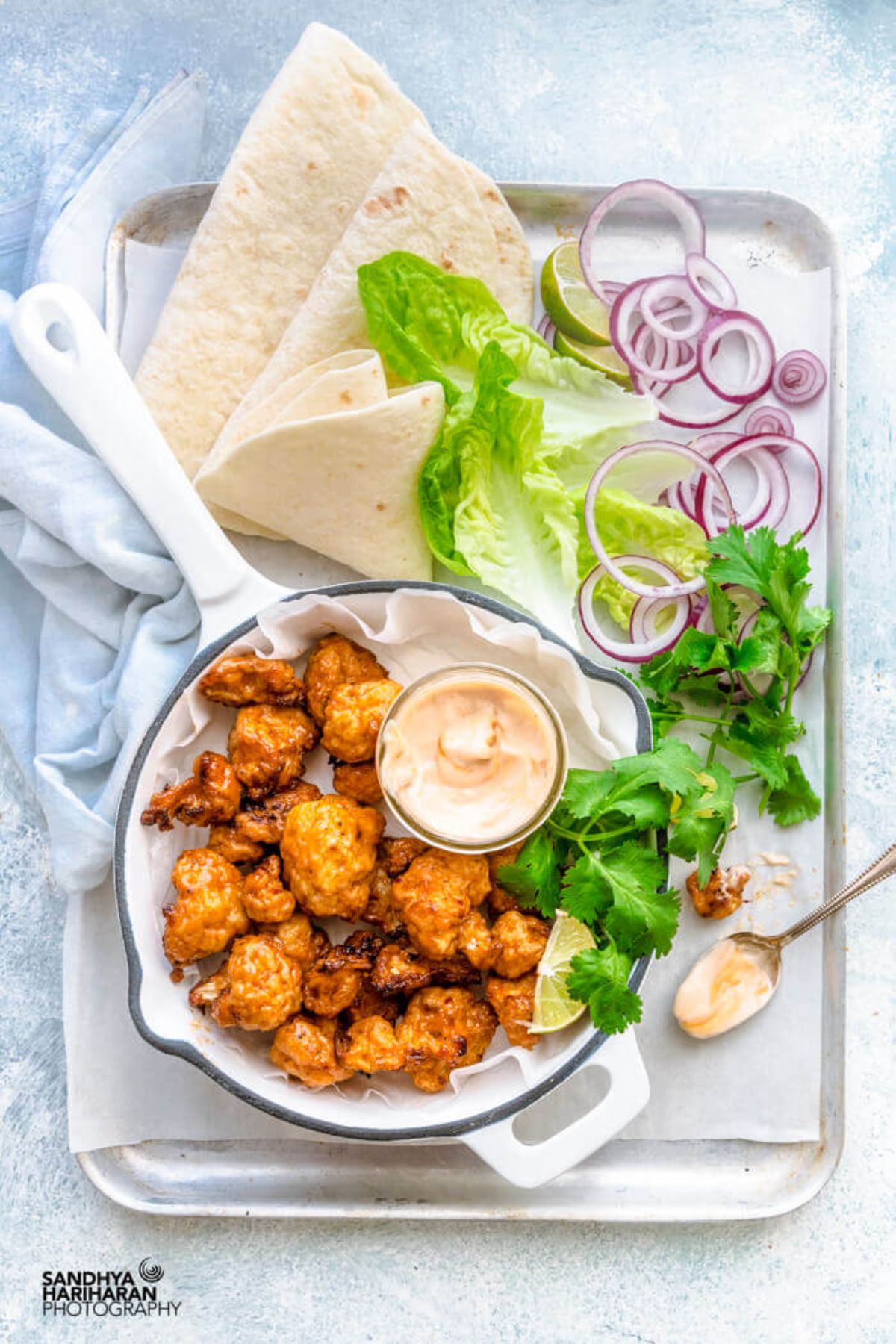 a tray laden with a cast iron pan full of cauliflower wings and dip, folded tortilla wraps, and salad