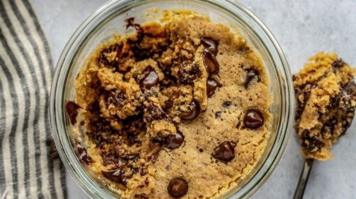 a glass bowl of cookie dough, with a spoon holding cookie dough next to it
