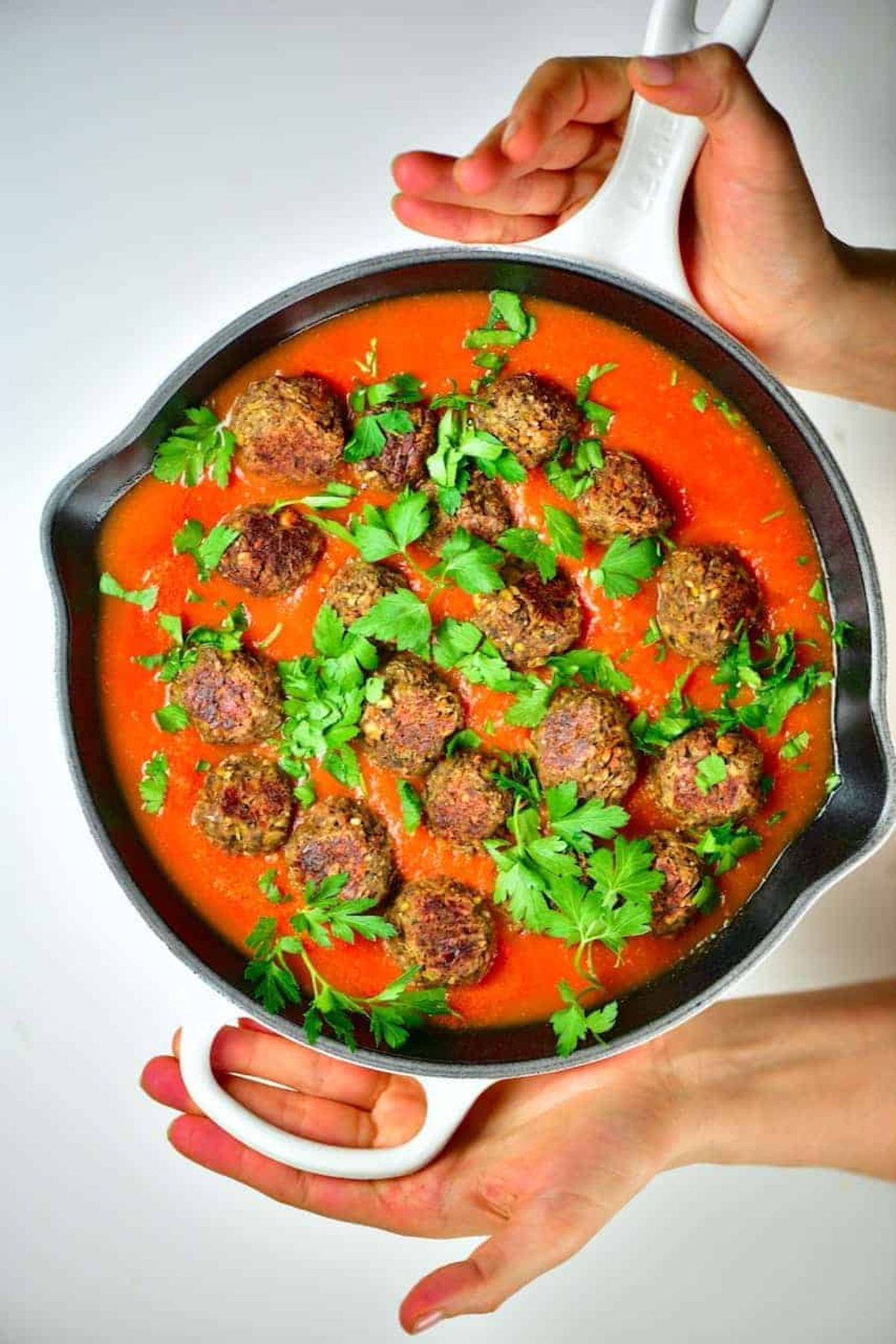 a cast iron skillet with lentil and mushroom vegan meatballs in tomato sauce, scattered with fresh herbs