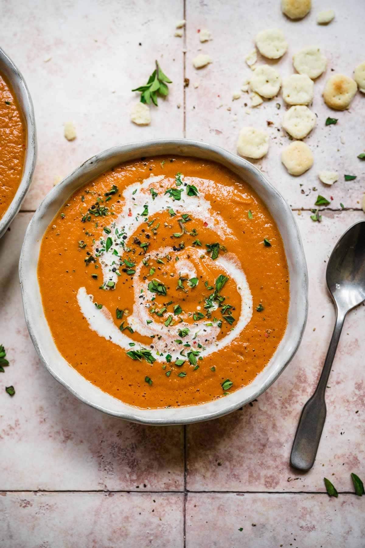 a hand crafted bowl full of tomato soup topped with vegan cream and chopped herbs