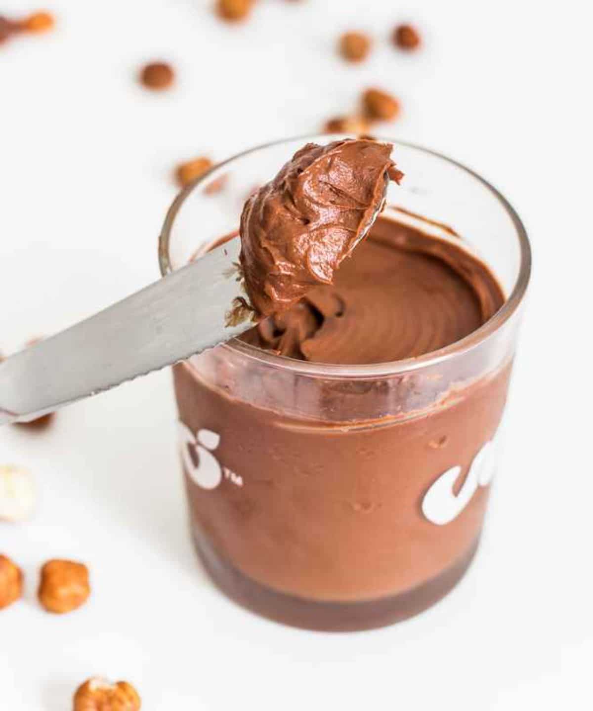 a glass jar of vegan nutella with a knife scooping some out fo the jar