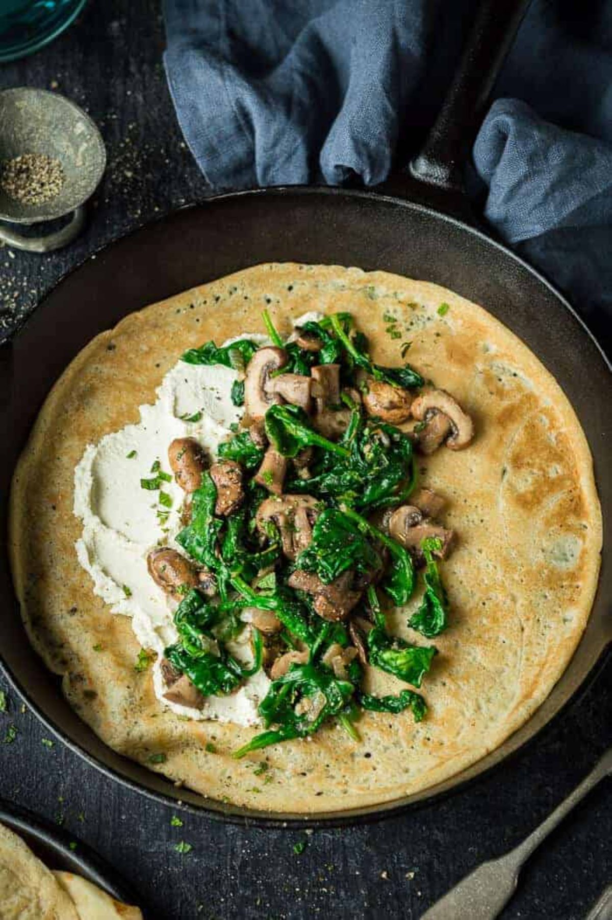 a cast iron skillet with a vegan crepe topped with mushroom and spinch