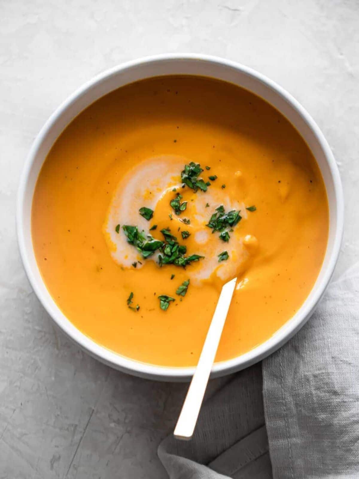 a white bowl of sweet potato soup topped with chopped herbs