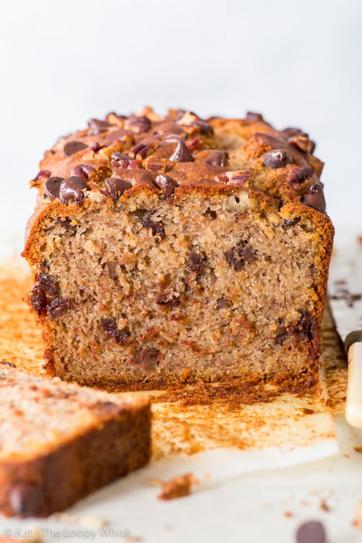 a loaf of vegan banana bread has been sliced open to reveal the inside. It is studded with chocolate chips