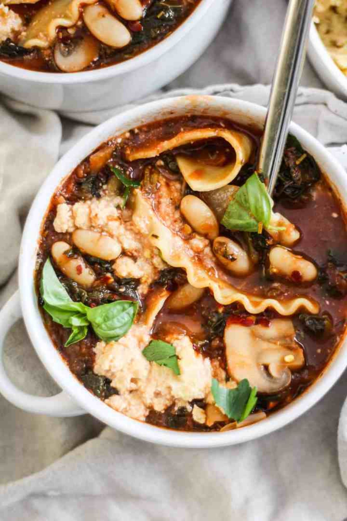 a white bowl of lasagne soup with a spoon sitting in it