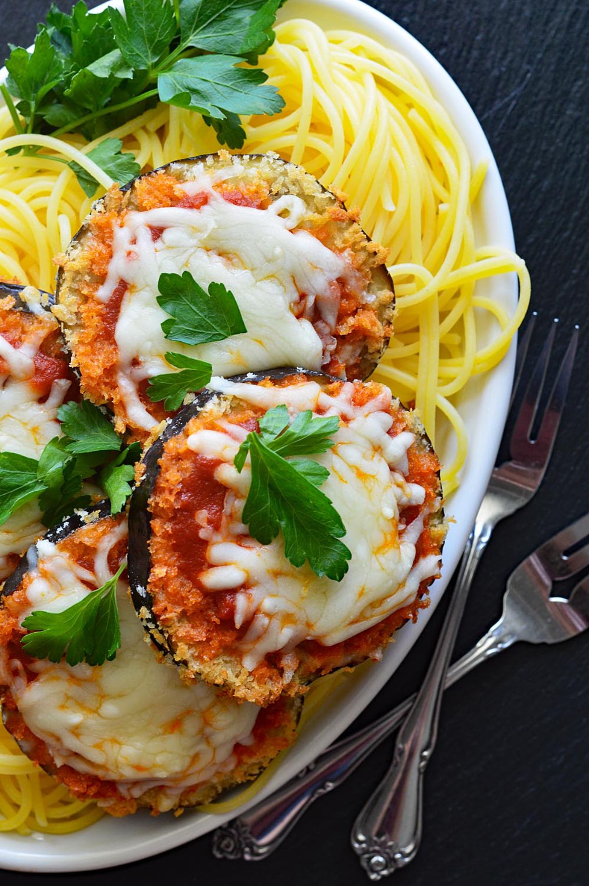 a plate full of eggplant parmesan on a bed of spaghetti
