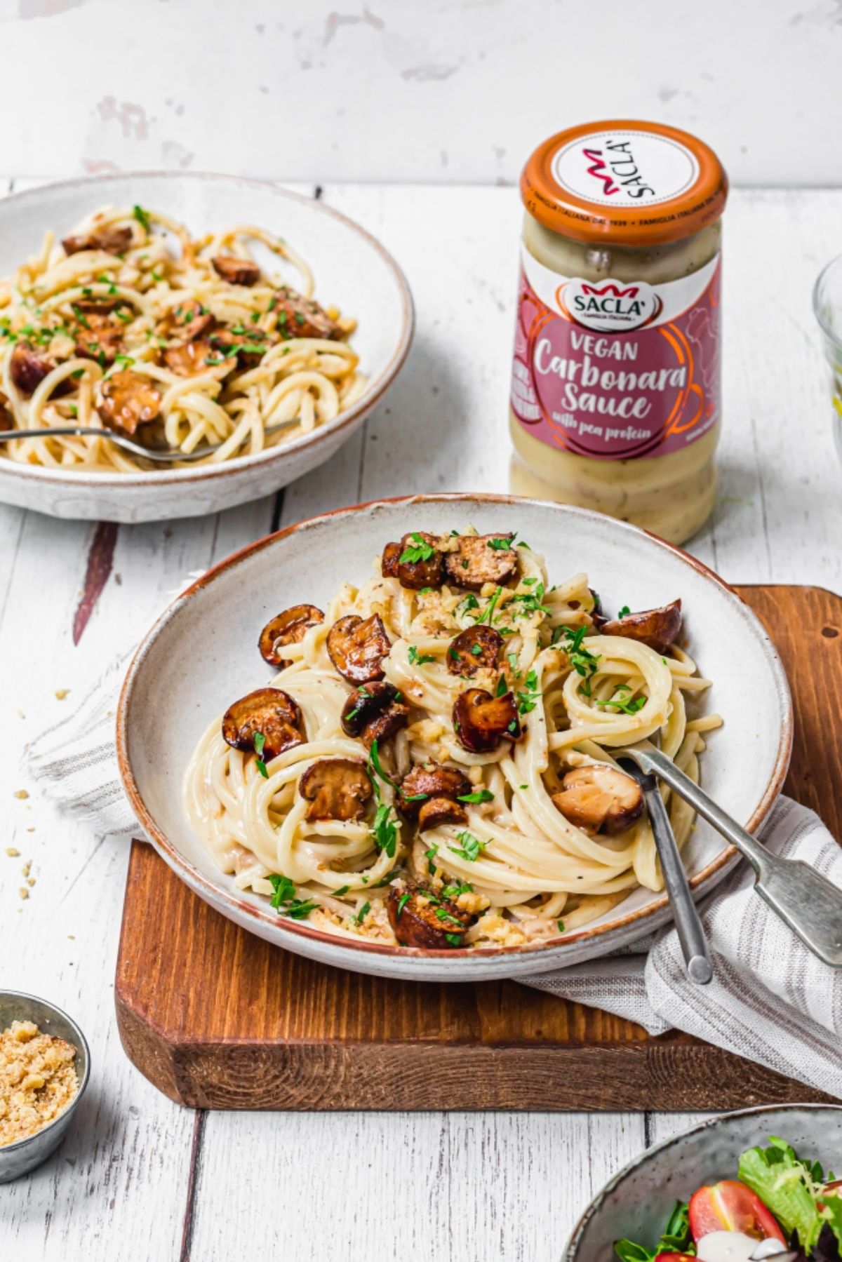 2 bowls of vegan carbonara with marinated mushrooms with a jar of vegan carbonara sauce to one side