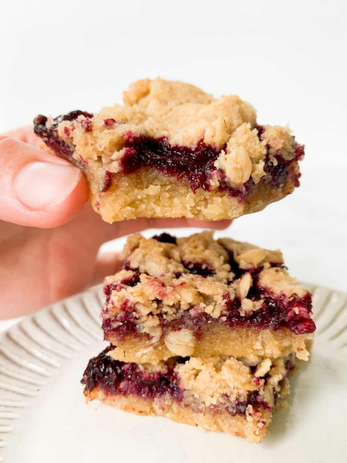a stack of vegan berry crumbles. A hand holds one bar with a bite taken out of it