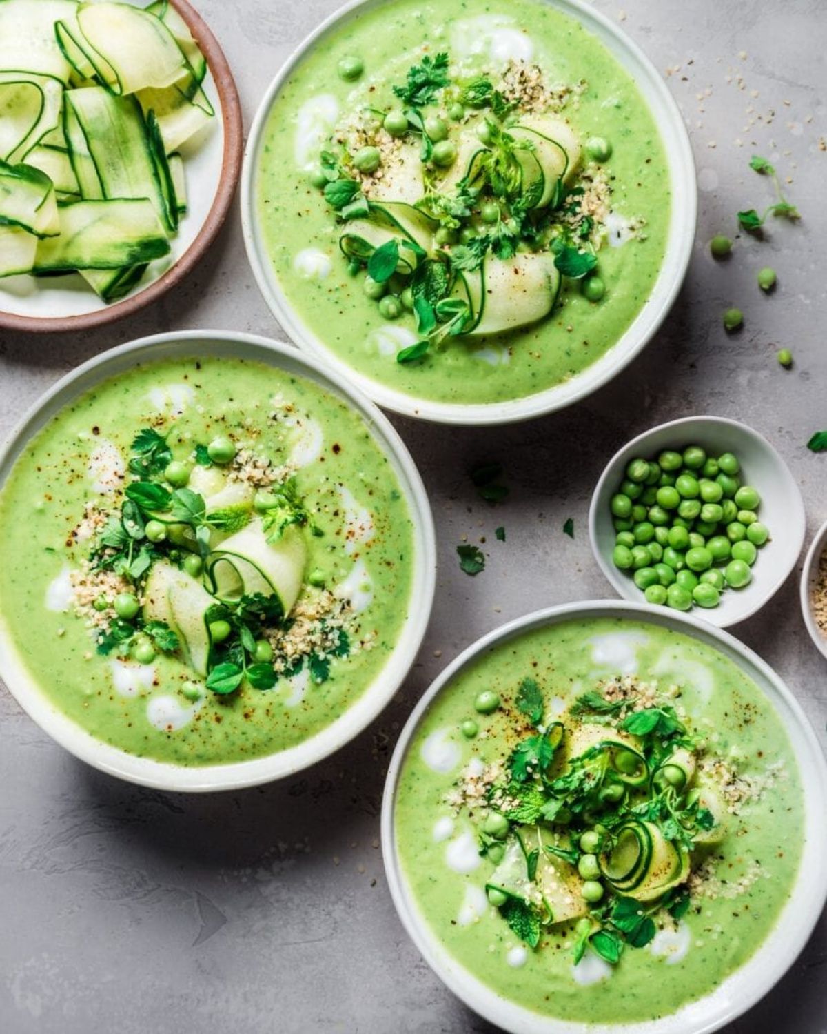 3 bowls of avocado gazpacho, topped with cucumer slices and peas.