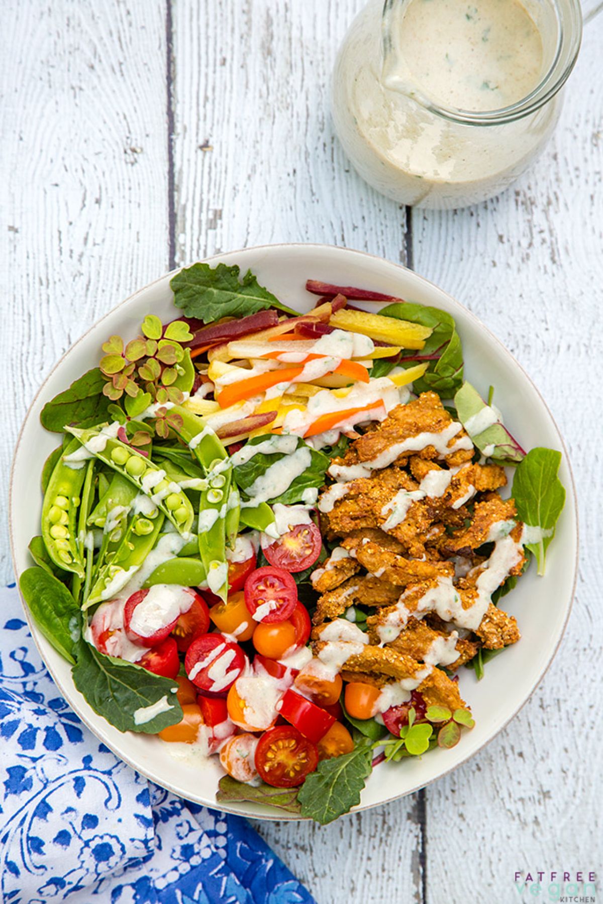 a white dish full of soy curls, green salad, and drizzled with salad dressing.