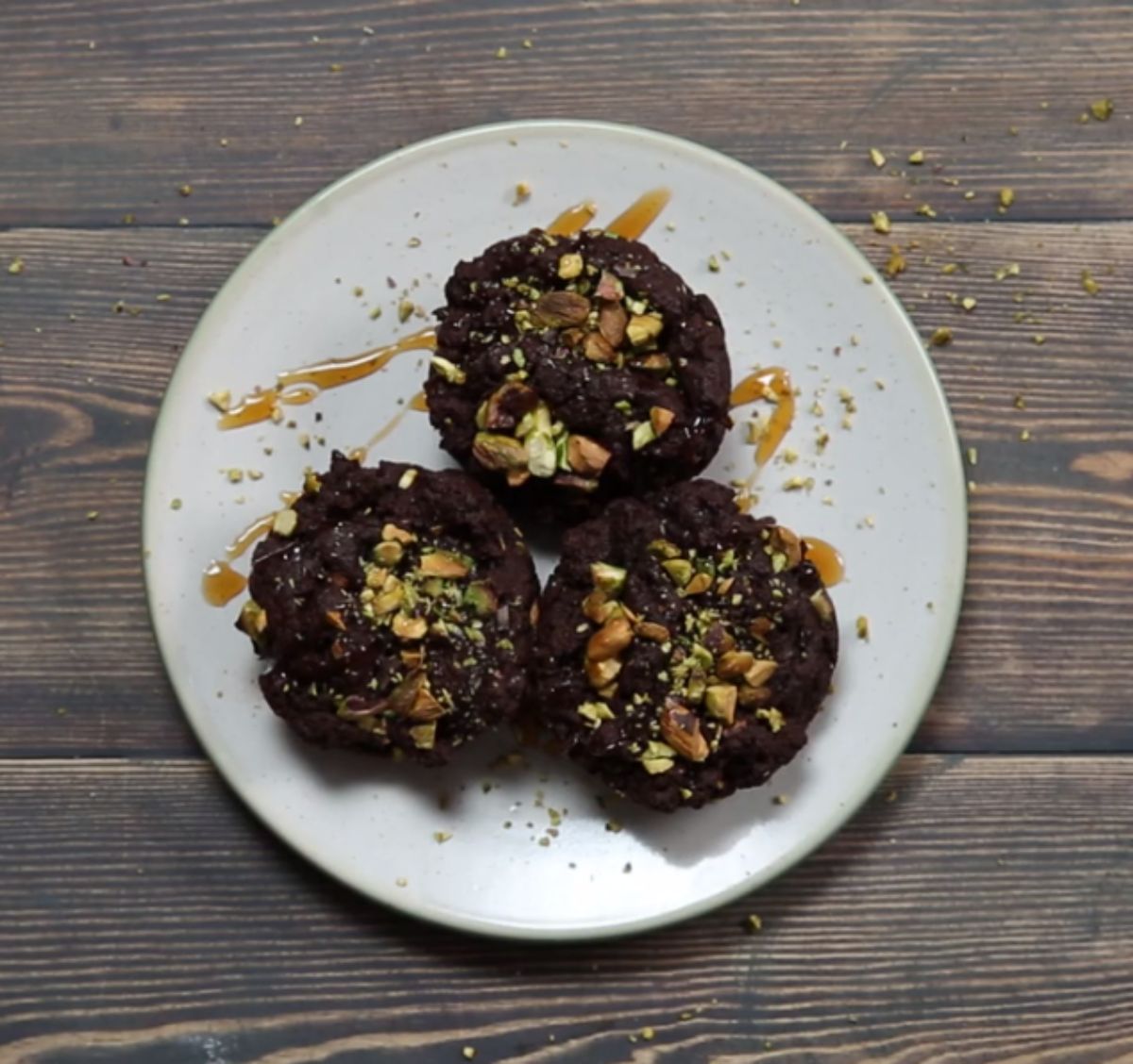 a white plate with 3 pistachio brownies on it, topped with chopped postachios and drizzled with caramel